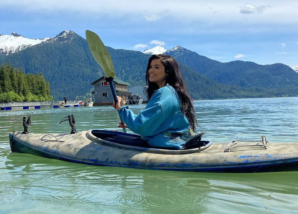 Keyana Pardilla, a young woman with long dark hair sitting in a canoe on the lake with mountains in the background 
